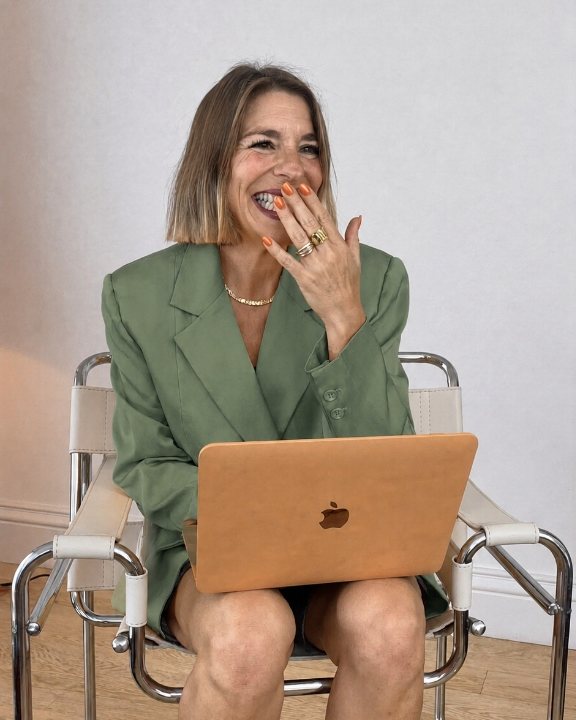 Julieta Bolullo riéndose, sentada con el portátil en las rodillas y americana verde